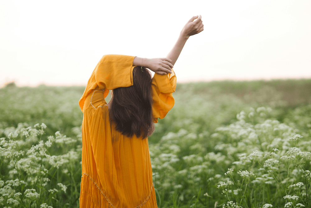 Una ragazza in un prato allunga le braccia in un gesto di apertura e respiro, simbolo del movimento consapevole e dell’ascolto del corpo nella vita quotidiana.