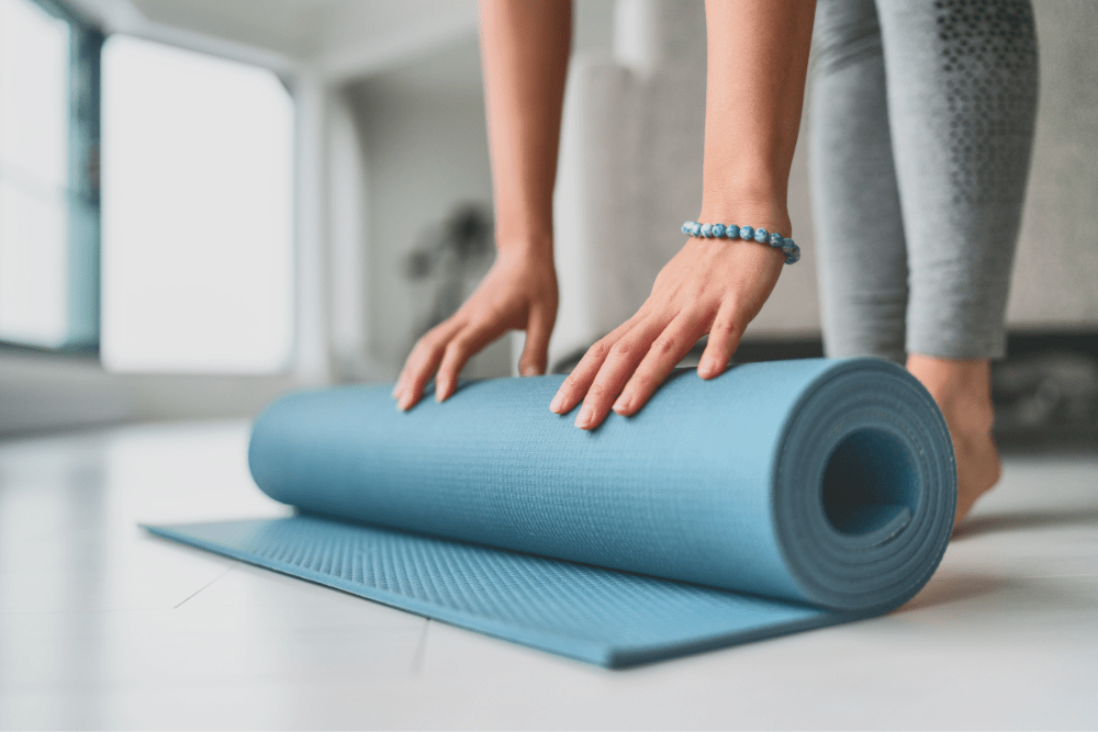 Primo piano di una mano femminile che srotola un tappetino yoga su pavimento in legno prima della pratica.